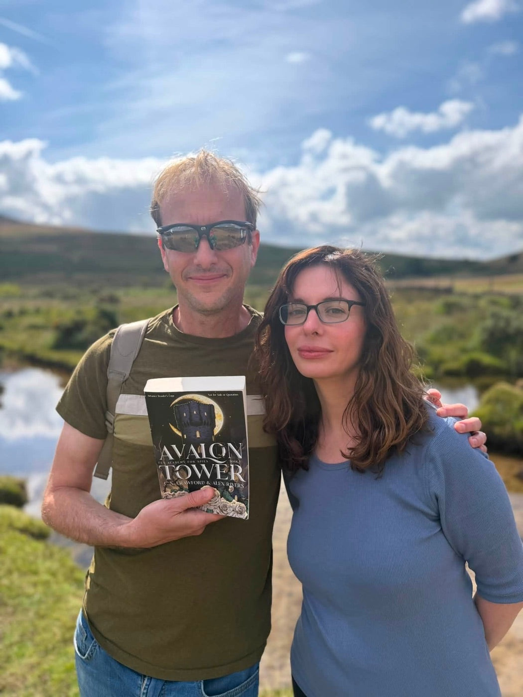 Alex and Christine outdoors, holding a copy of Avalon Tower